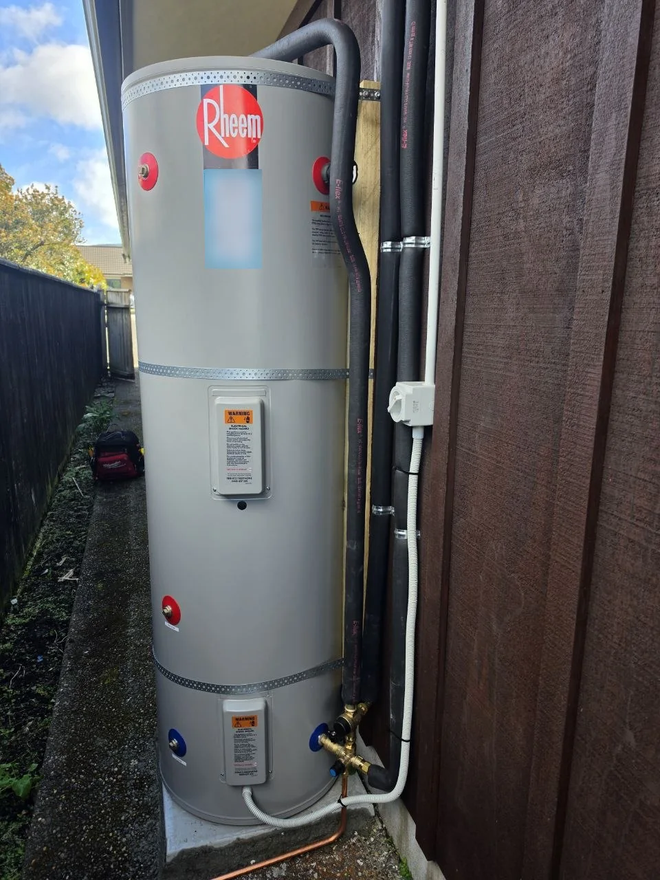 Outdoor Rheem cylinder beside a house, with insulated pipework and a concrete base